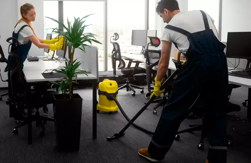 Personal aspirando la alfombra y limpiando escritorios de una oficina